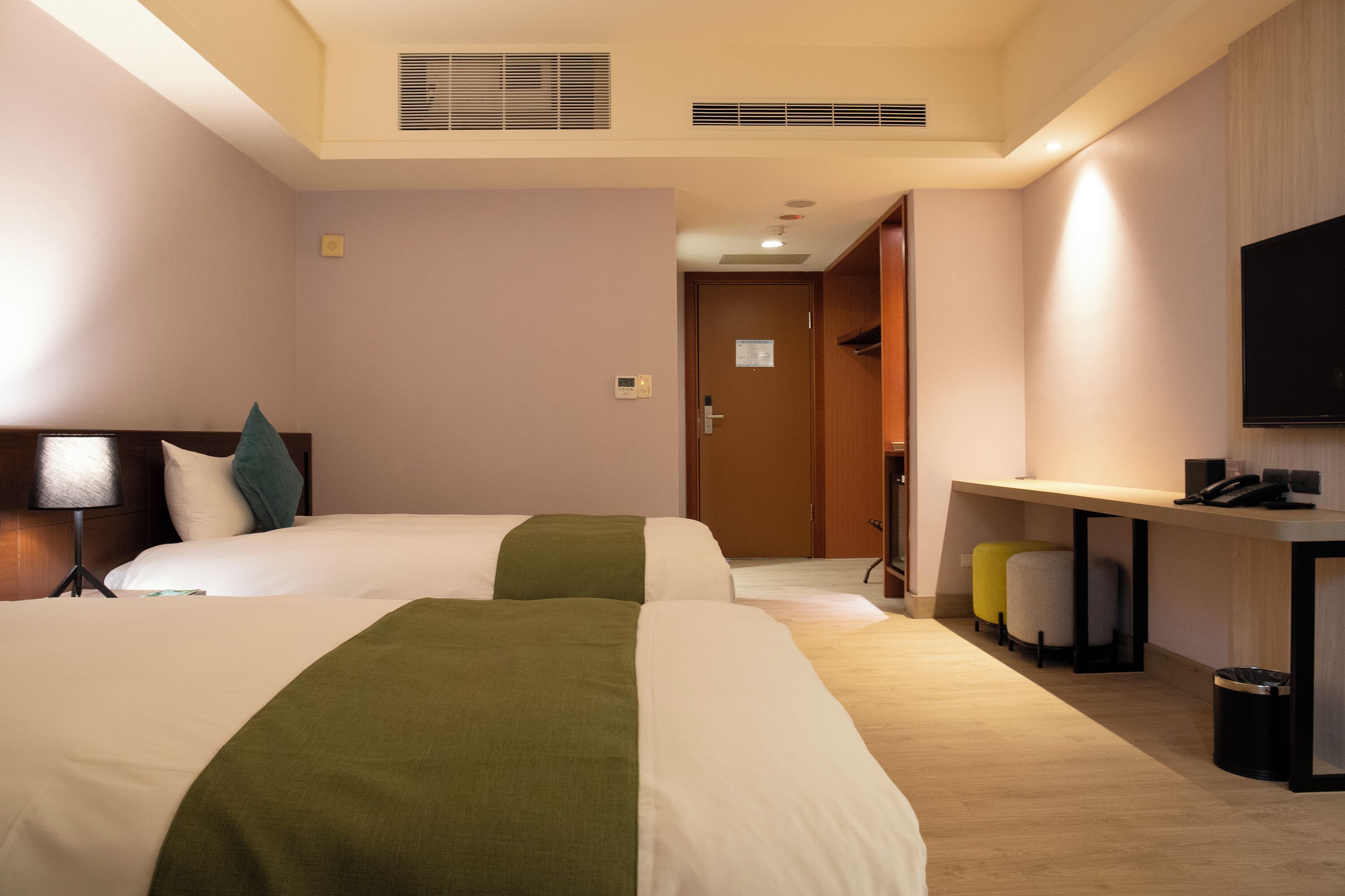 A hotel room with two beds, a desk, a TV, and a trash bin.