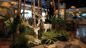 A lobby with a central decorative area featuring a large deer sculpture surrounded by tropical plants and hanging wicker lamps. - Aspire Resort (Taoyuan City)