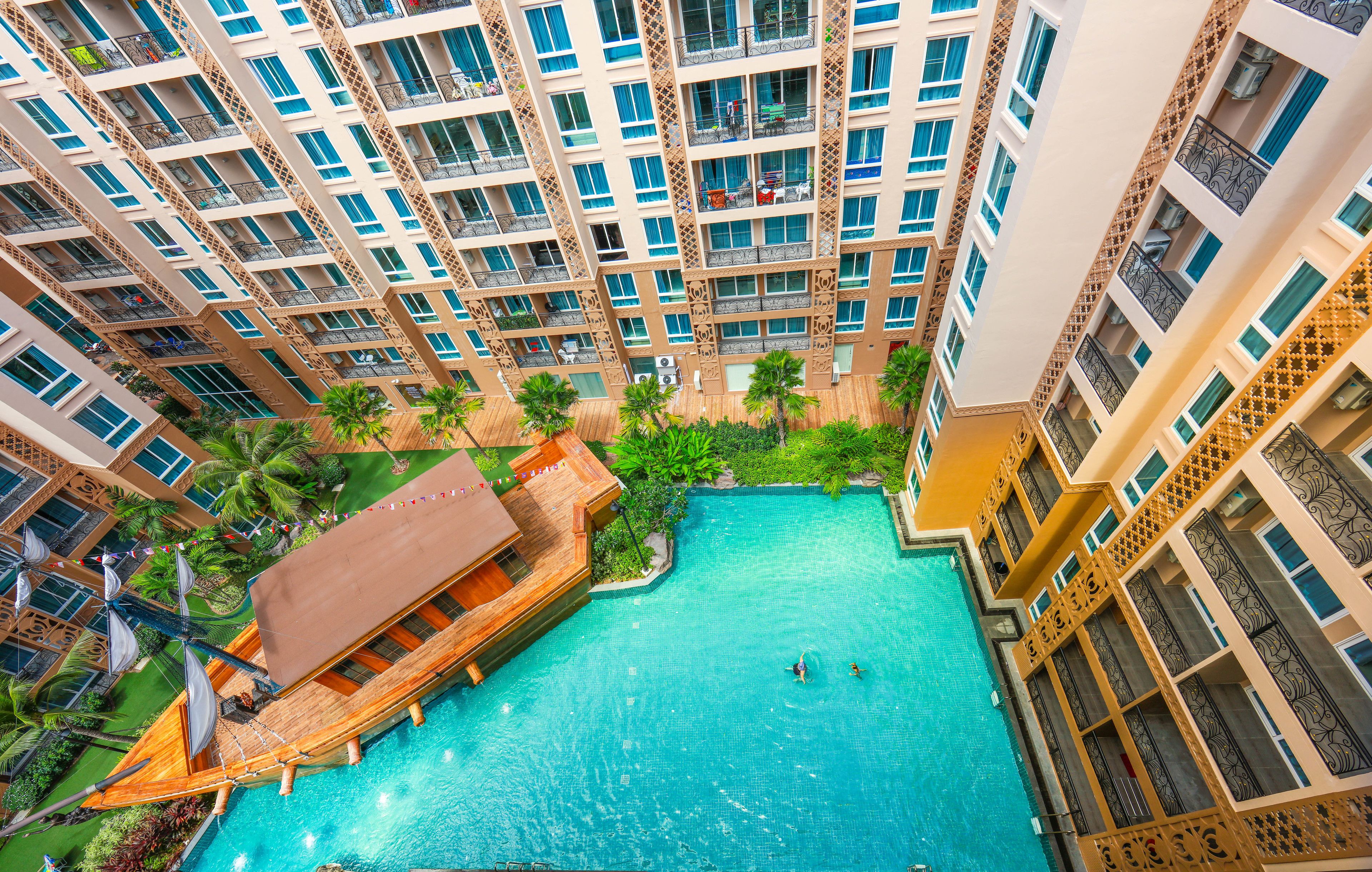 Un hotel moderno de gran altura con varias terrazas, una piscina central y abundante vegetación.