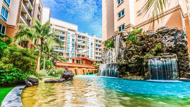 A hotel courtyard with a clear pool, a waterfall, and lush greenery. - Atlantis Condo Resort by Natnarin (Pattaya)