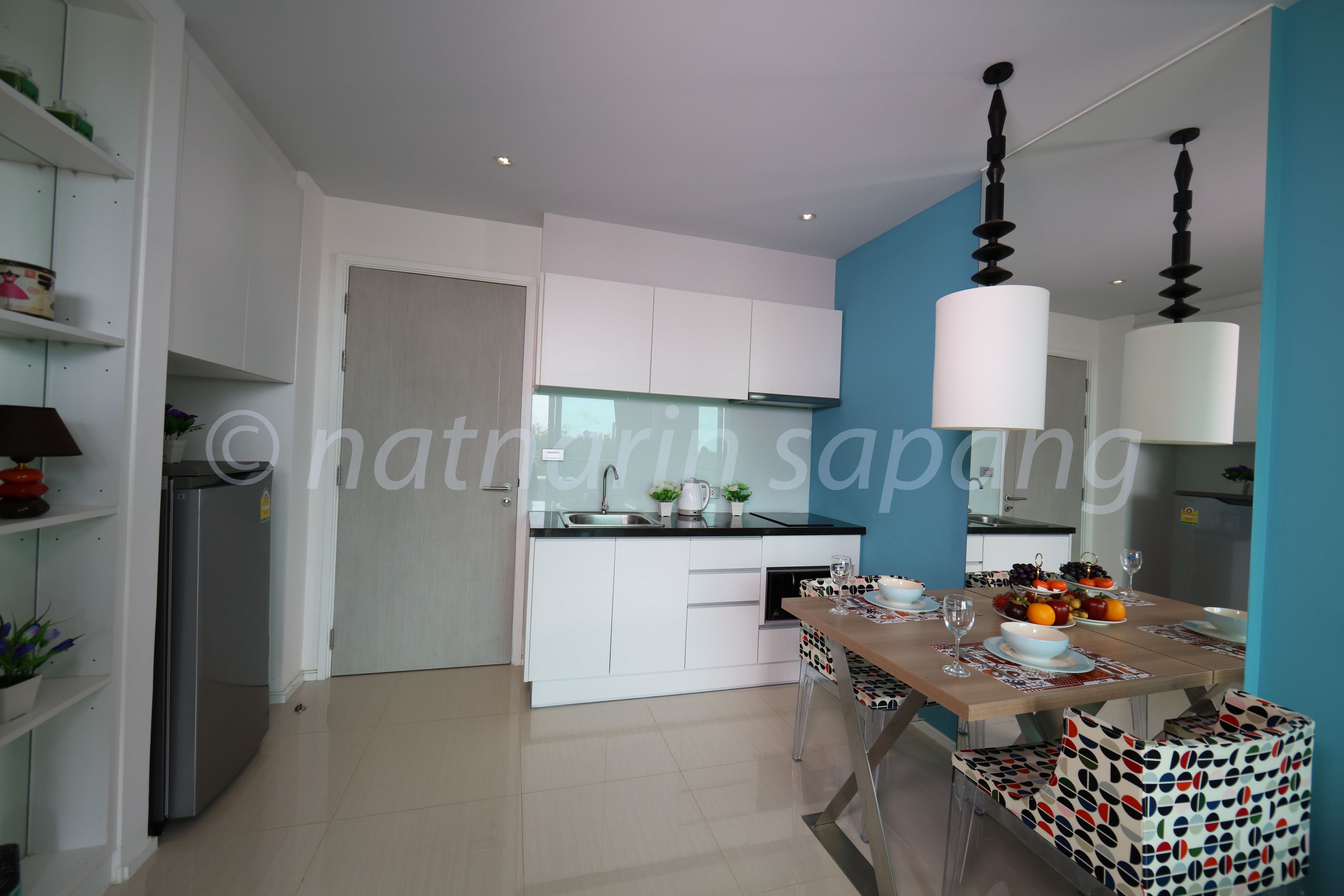 A modern kitchen with white cabinets, a stainless steel refrigerator, and a dining area with a wooden table and patterned chairs.