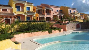 A resort with a swimming pool, colorful buildings, and a clear sky. - Residenza Zodiaco (Santa Teresa di Gallura)