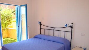 A bedroom with a bed, a nightstand, and a window with an open door leading to a garden. - Residenza Zodiaco (Santa Teresa di Gallura)