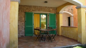 A patio with a table and chairs, stone walls, and green shutters. - Residenza Zodiaco (Santa Teresa di Gallura)