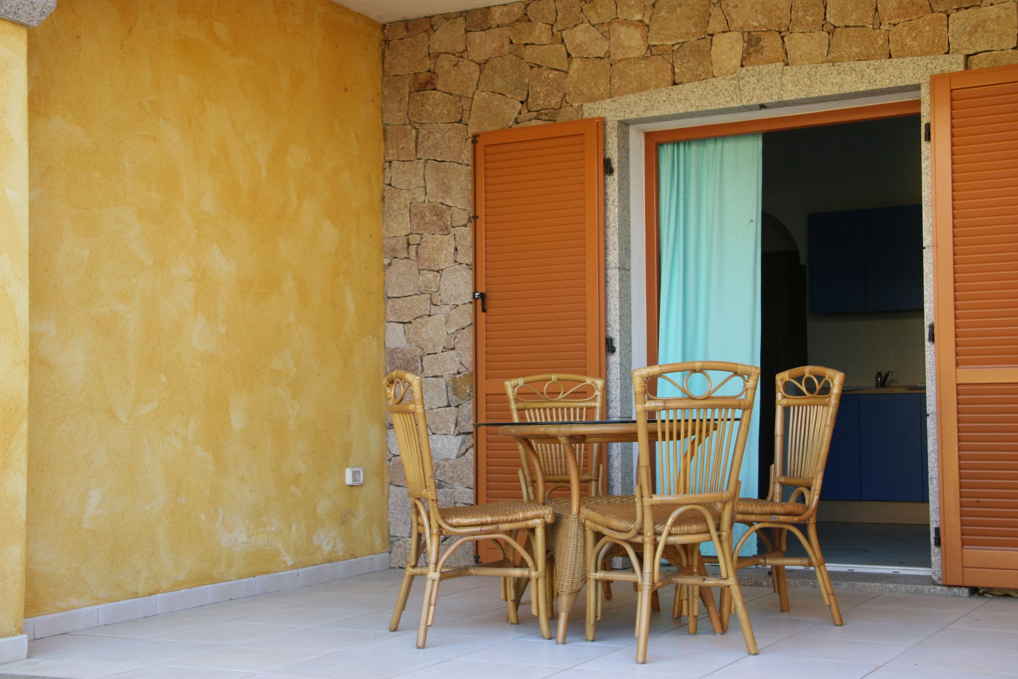 A dining area with a stone wall, wooden shutters, and wicker furniture.