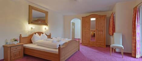 A bedroom with a wooden bed, a nightstand, a mirror, a wardrobe, and a chair.
