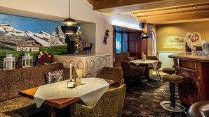 Restaurante com vigas de madeira, um mural com paisagem de montanha e um espaço de bar com banquetas.