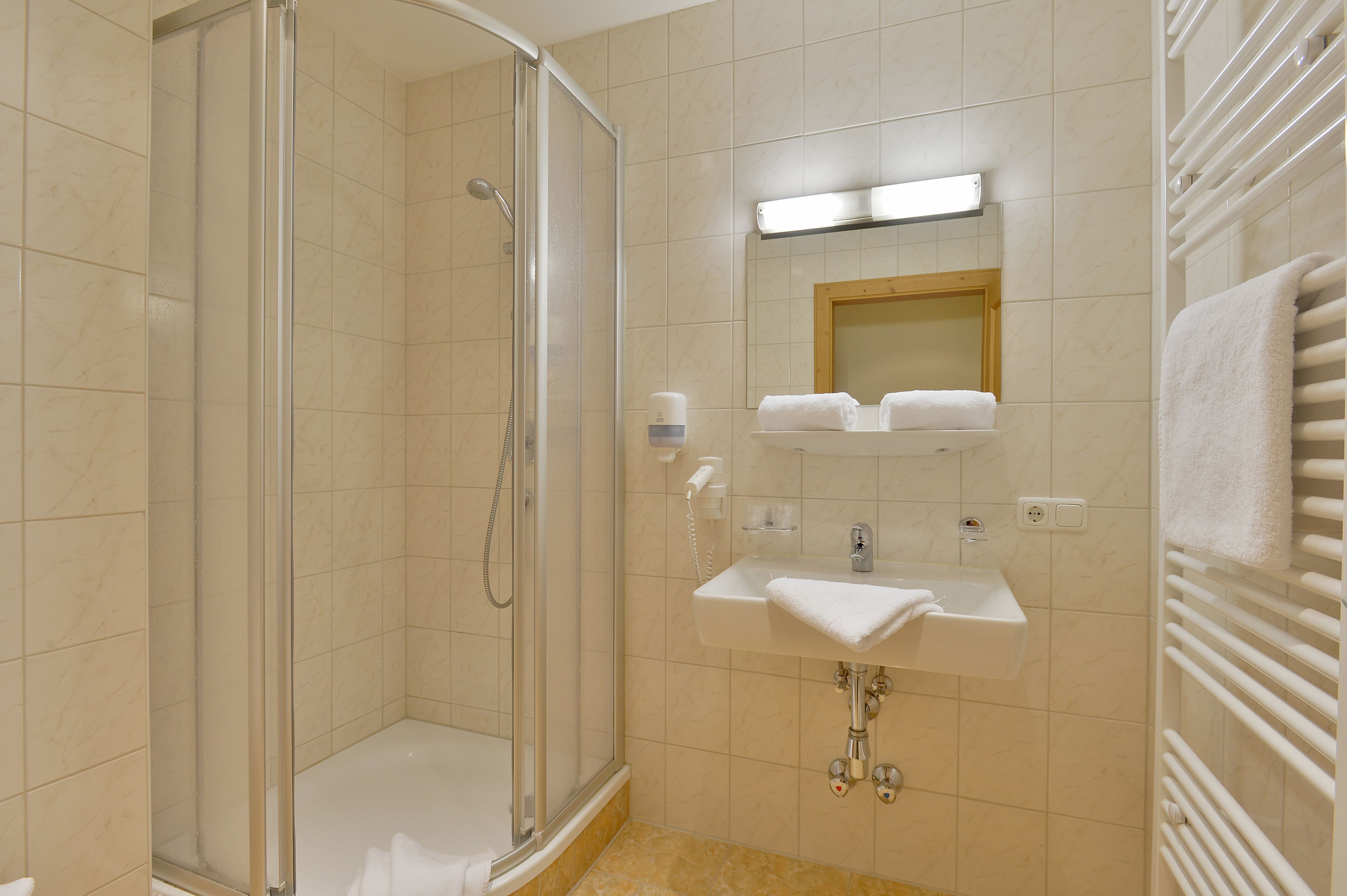 Un baño moderno con ducha de vidrio, lavamanos con espejo y un perchero para toallas.