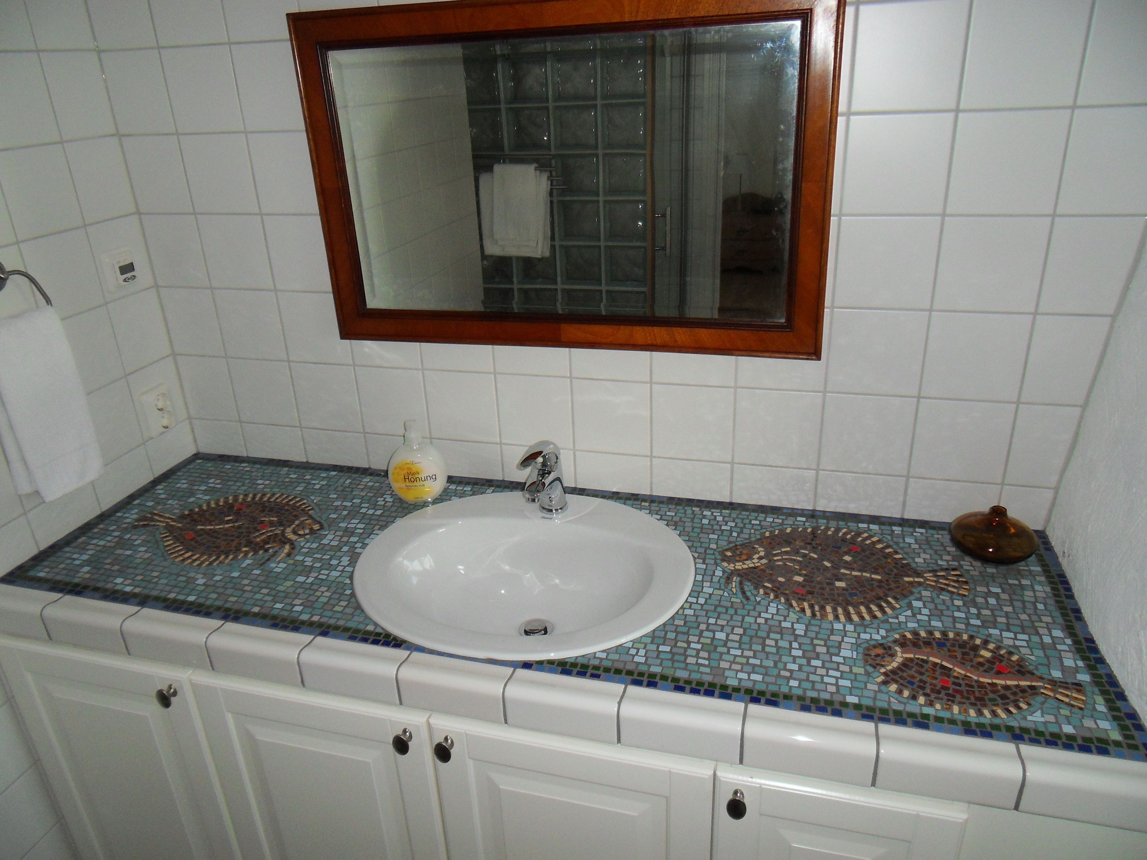 A bathroom with a white sink, a mirror with a wooden frame, and a tiled backsplash with a fish pattern.