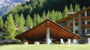 A lodge with a wooden roof structure, outdoor seating, and a mountain backdrop. - Notre Maison Eco Wellness Hotel (Cogne)