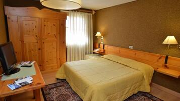 Una camera d'albergo con un letto in legno, una scrivania con un computer, una lampada e un armadio.
