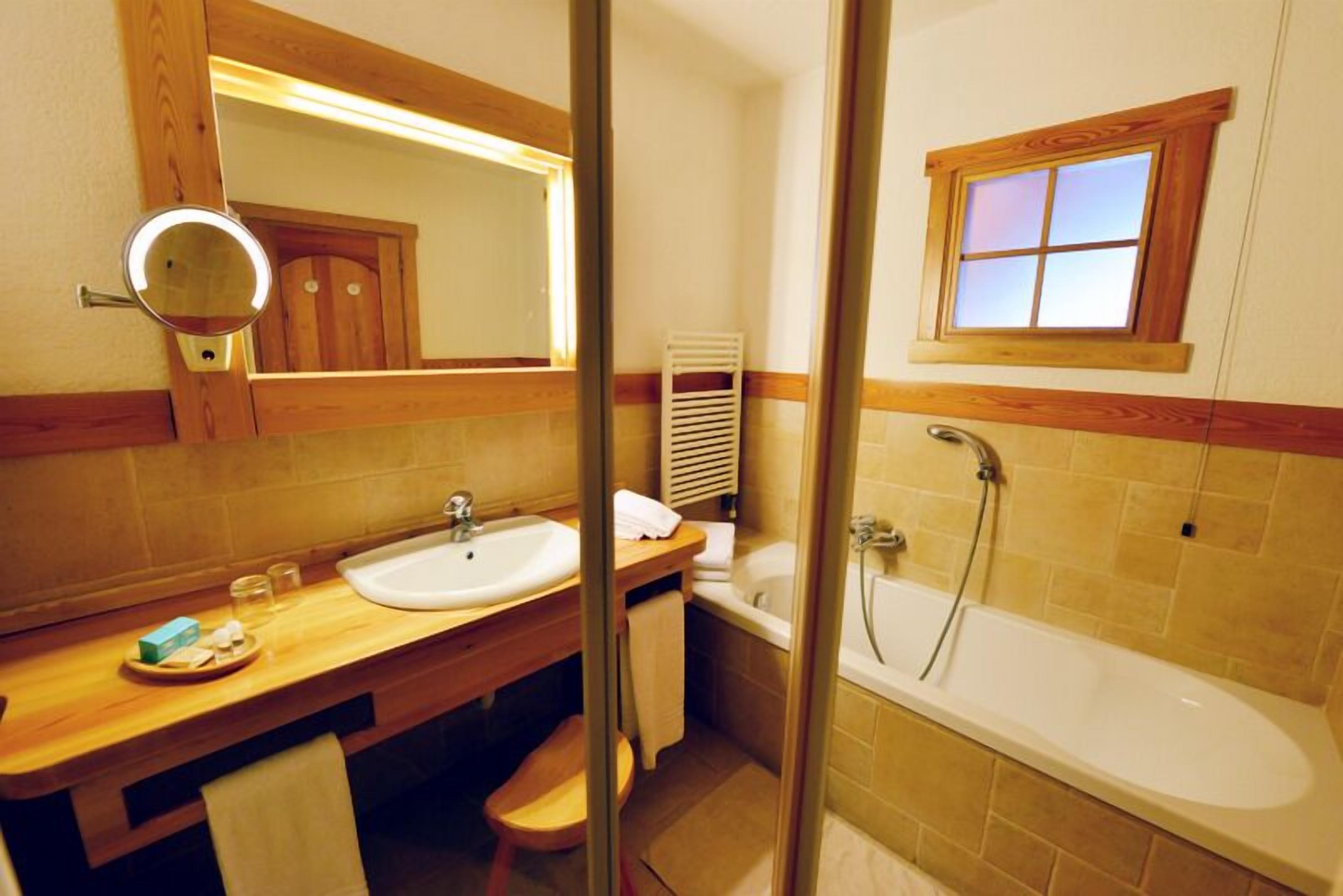 Un bagno con mobile bagno in legno, un lavandino, uno specchio, un porta asciugamani, una doccia e una finestra.