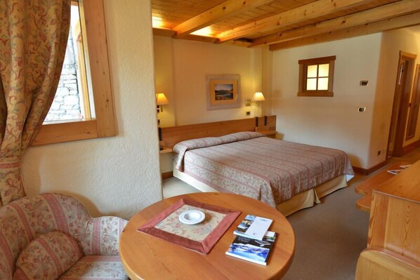 Una habitación acogedora con una cama grande, un pequeño sofá, una mesa redonda con una bandeja y dos lámparas de noche.