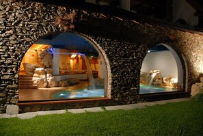 Un área de spa al aire libre con piscina, arcos de piedra y una cascada.
