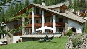 A chalet-style building with a stone facade, wooden balconies, and a well-maintained lawn with outdoor seating. - Notre Maison Eco Wellness Hotel (Cogne)