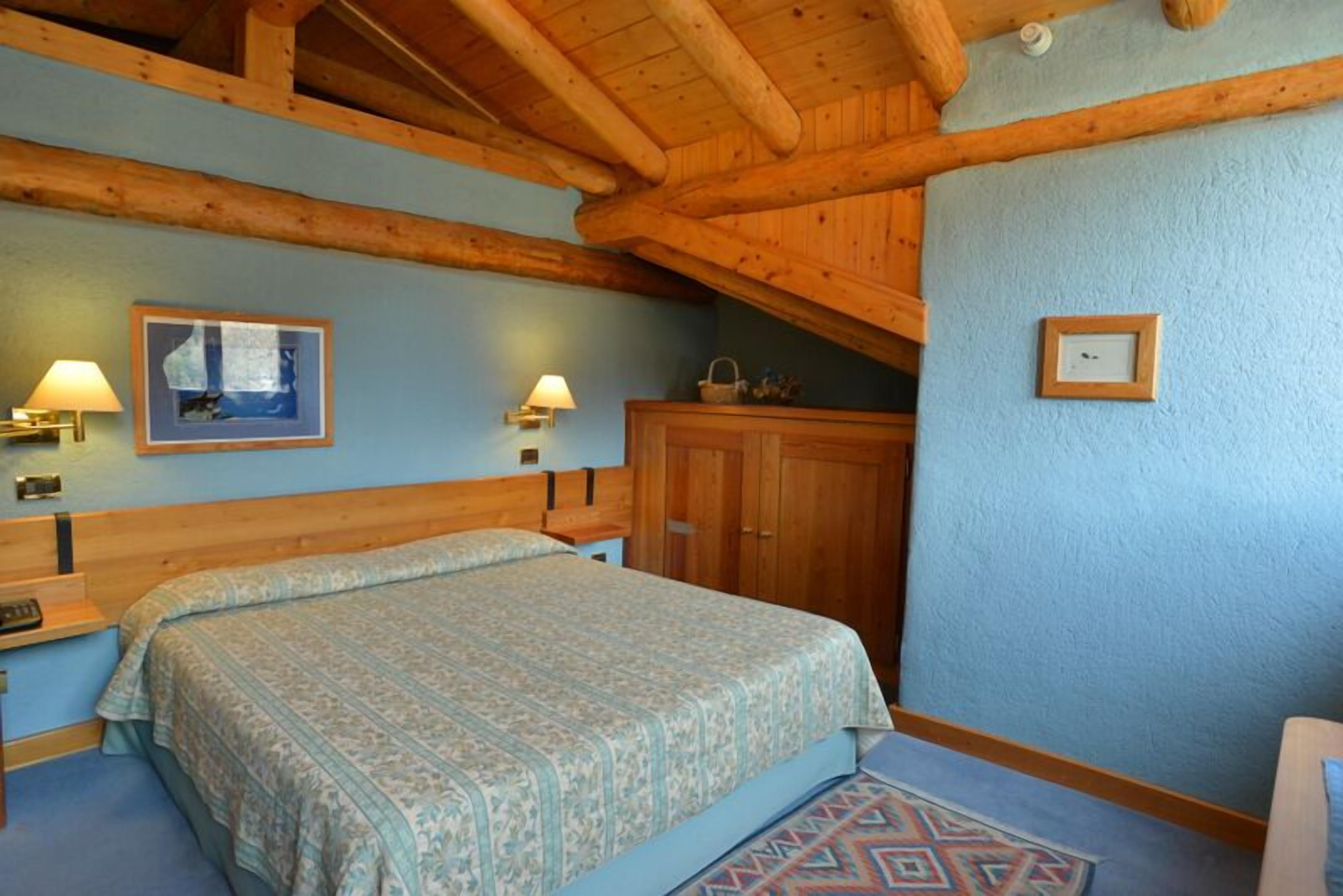 Una camera da letto con soffitto in legno, un letto con biancheria a motivi, due lampade a parete e una piccola cornice con un'immagine.