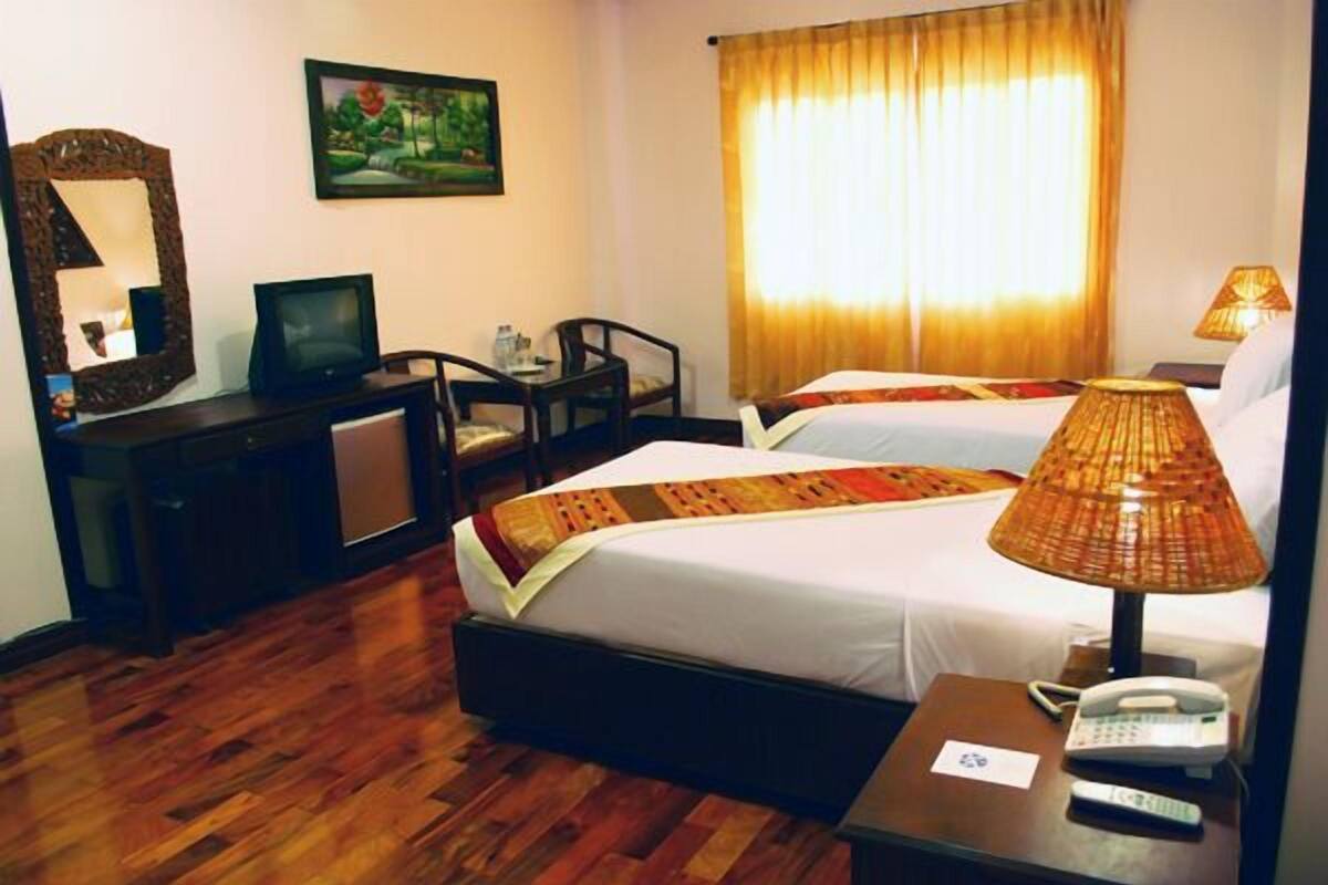 A hotel room with a bed, bedside table, lamp, and a desk with a television.