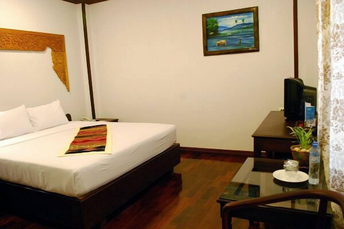 A hotel room with a bed, a desk, a chair, a television, and a painting on the wall.