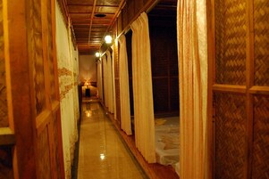 Un pasillo estrecho con paredes de madera y suelo pulido, que conduce a una habitación con cama y lámpara.