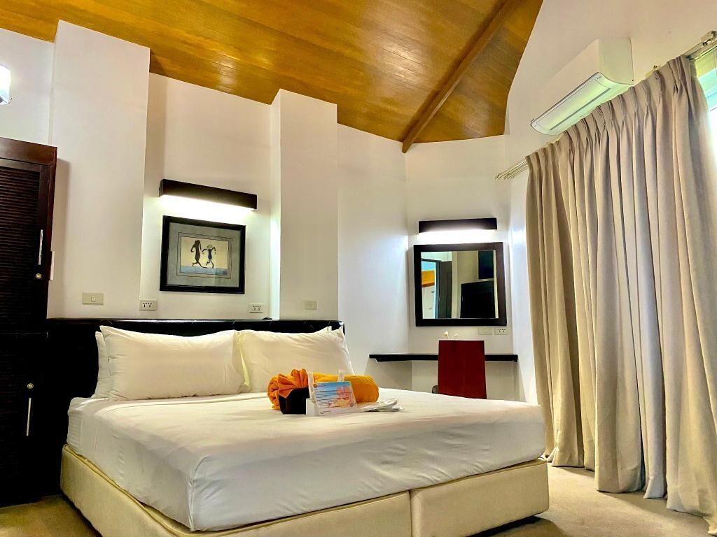 Quarto de hotel com cama, mesa de cabeceira, espelho, quadro e janela com cortinas.