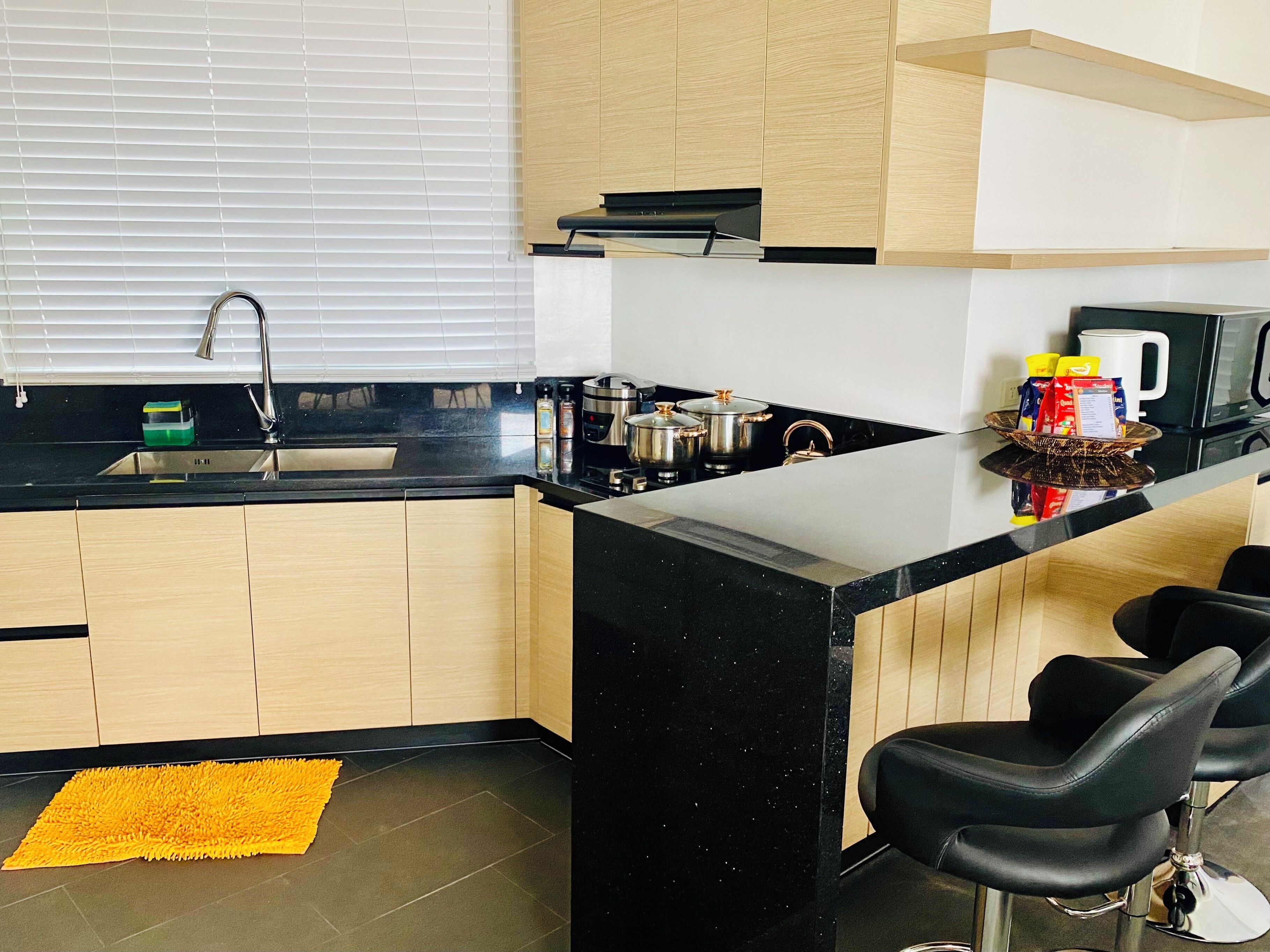 A modern kitchen with a black countertop, wooden cabinets, a stainless steel sink, and a yellow rug.