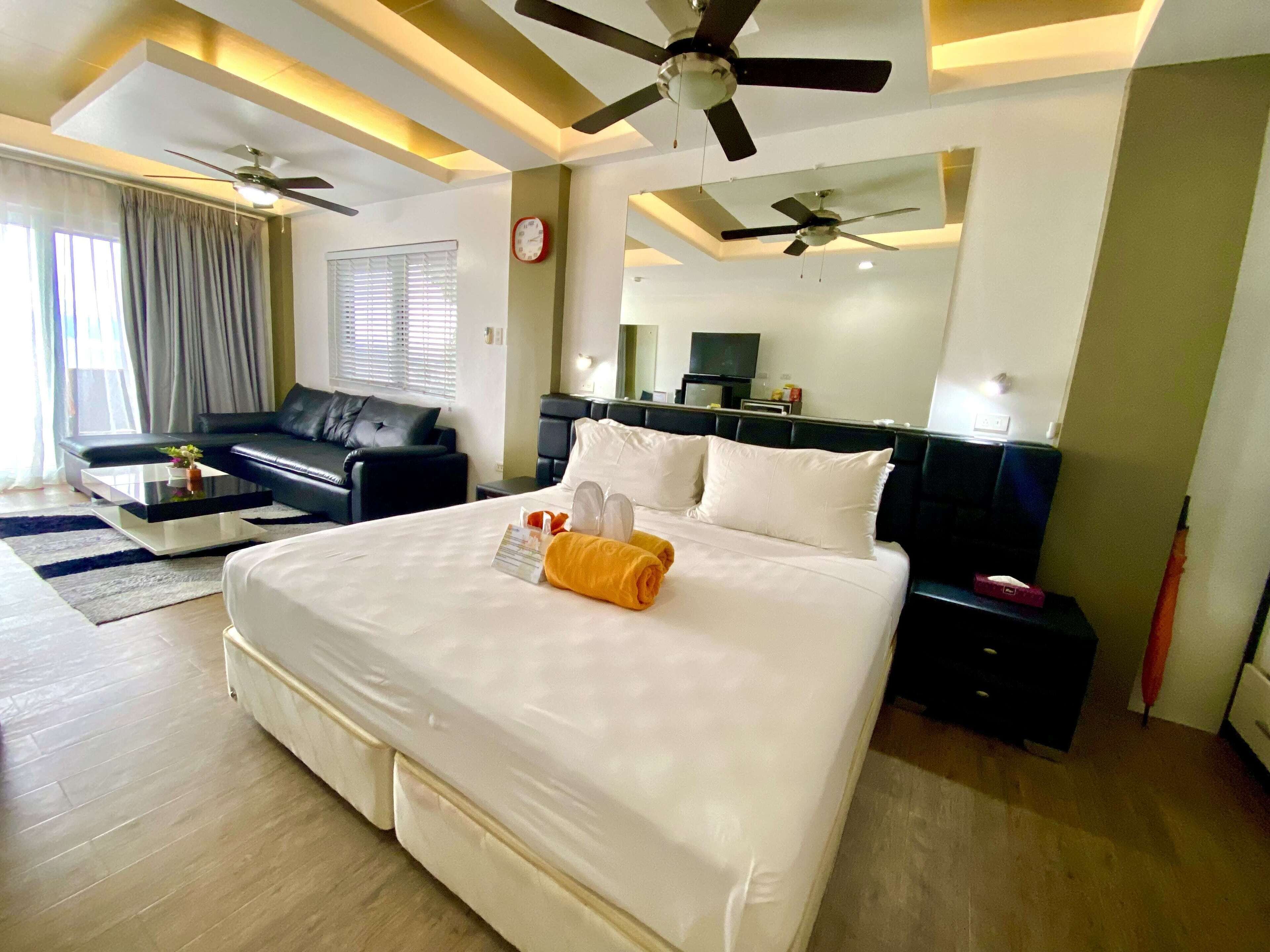 A hotel room with a large bed, a sofa, a desk, and a ceiling fan.