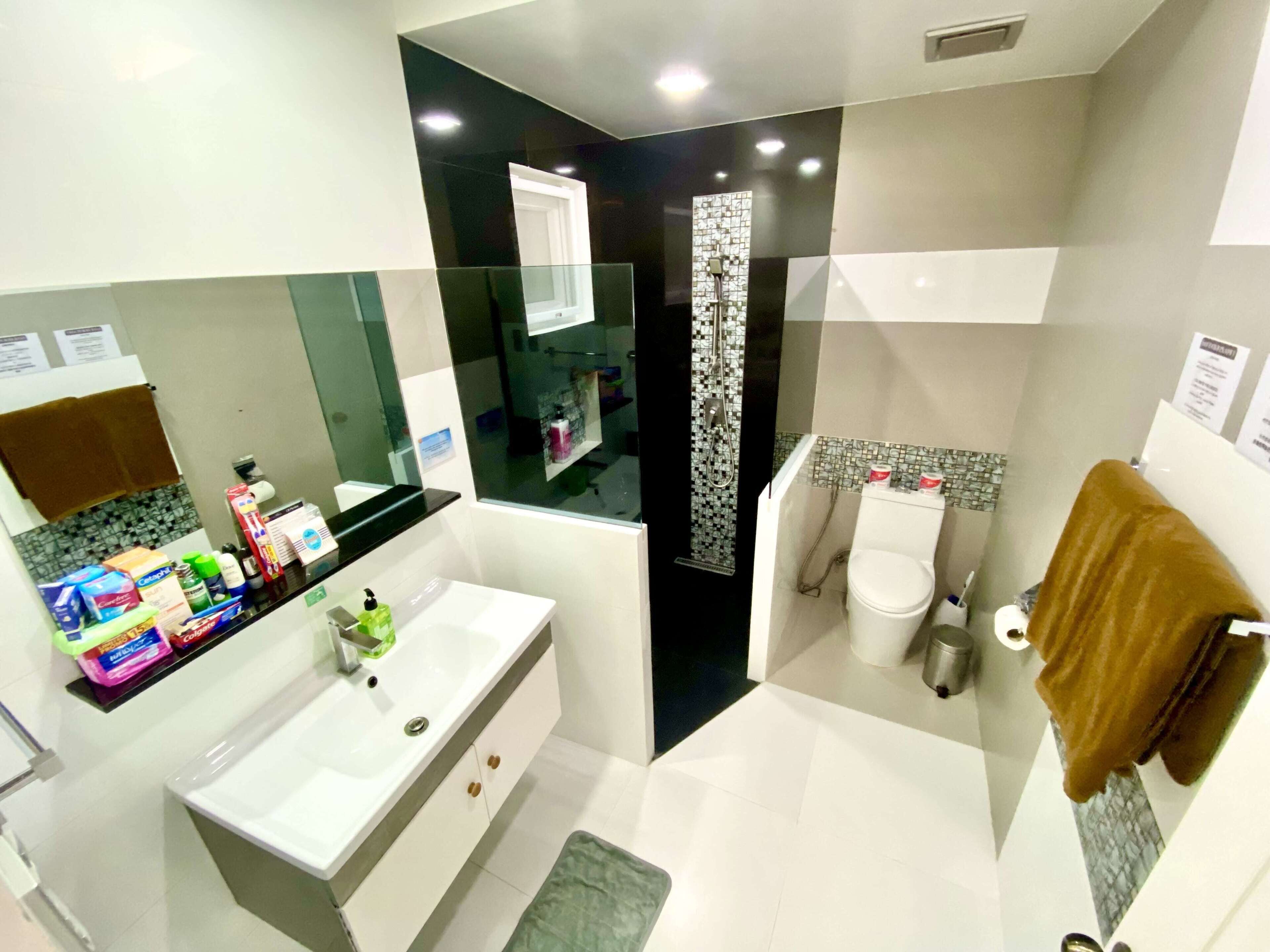 A modern bathroom with a white sink, a mirror, a shower, and a toilet.