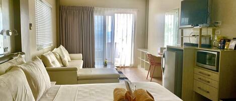 Una habitación de hotel con cama, escritorio, televisor y ventilador de techo.