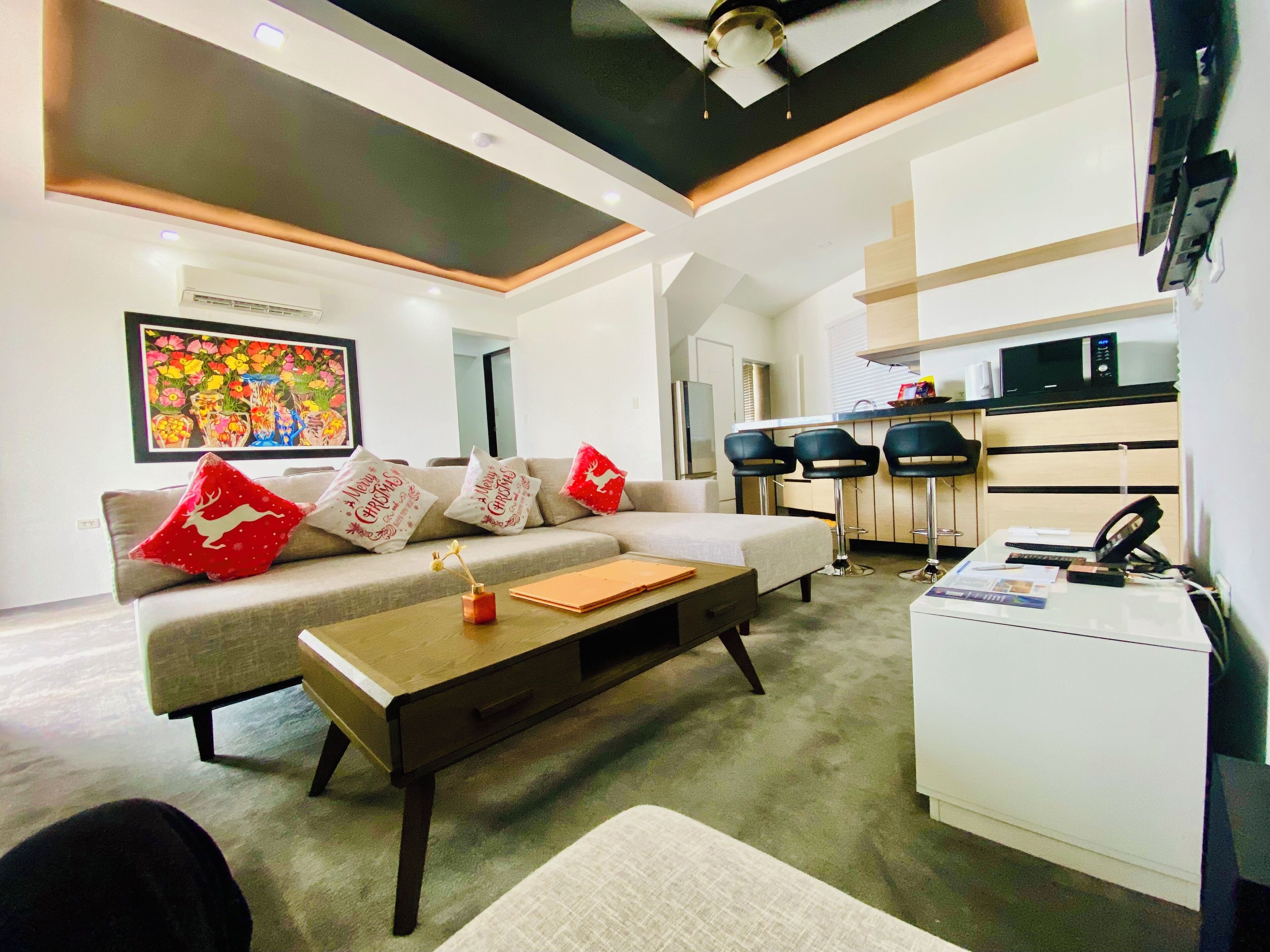 A modern living room with a sofa, coffee table, and a kitchen area with a microwave and bar stools.