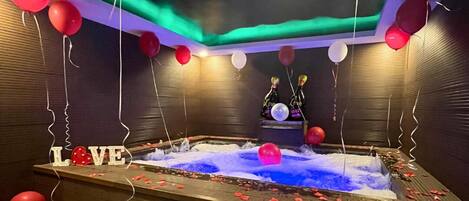 A hot tub with red balloons, a 'LOVE' sign, and champagne bottles.