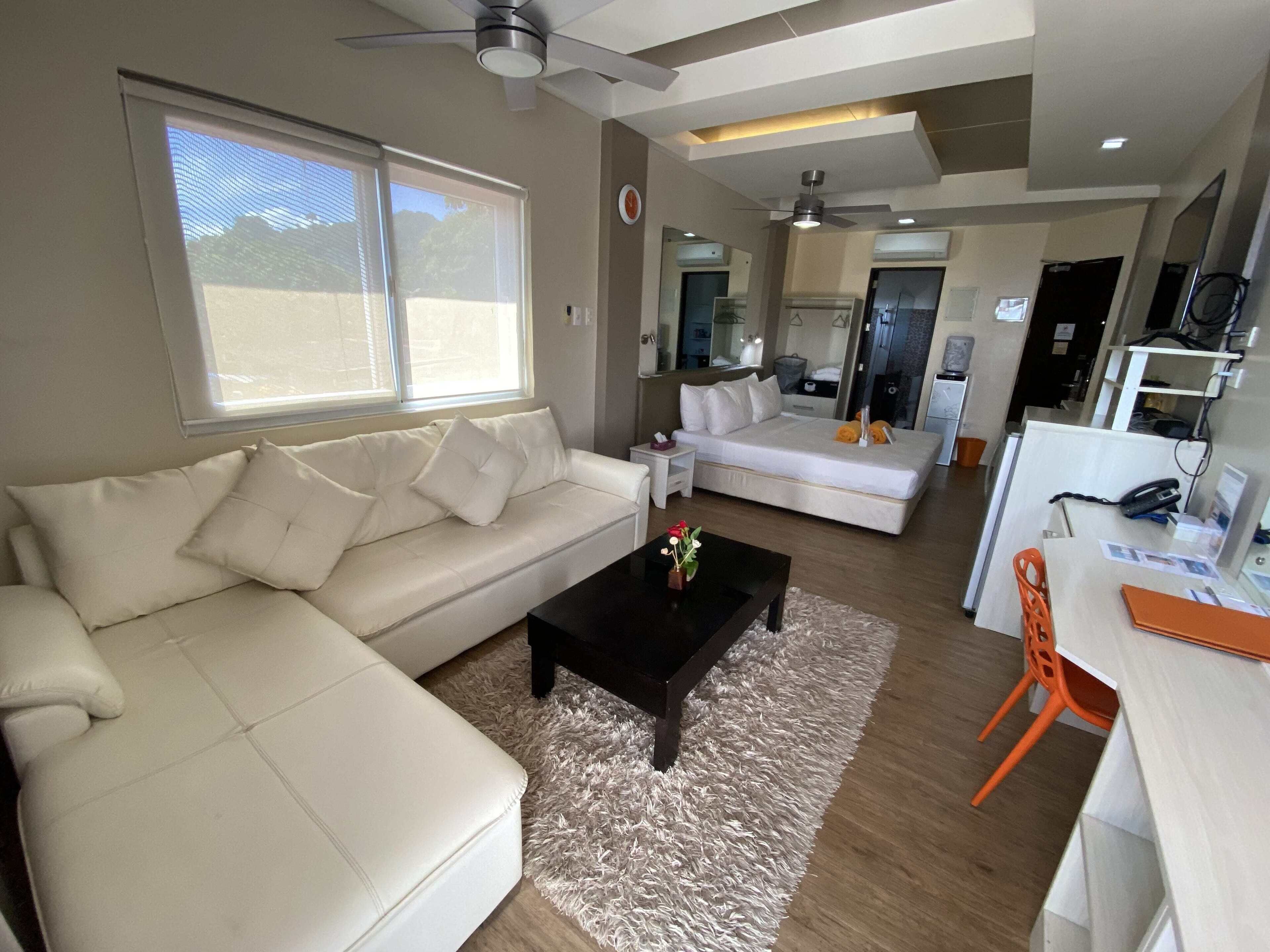 Un salon moderne avec un canapé blanc, une table basse noire et un tapis moelleux. On y trouve également un coin repas avec une table blanche et des chaises orange.