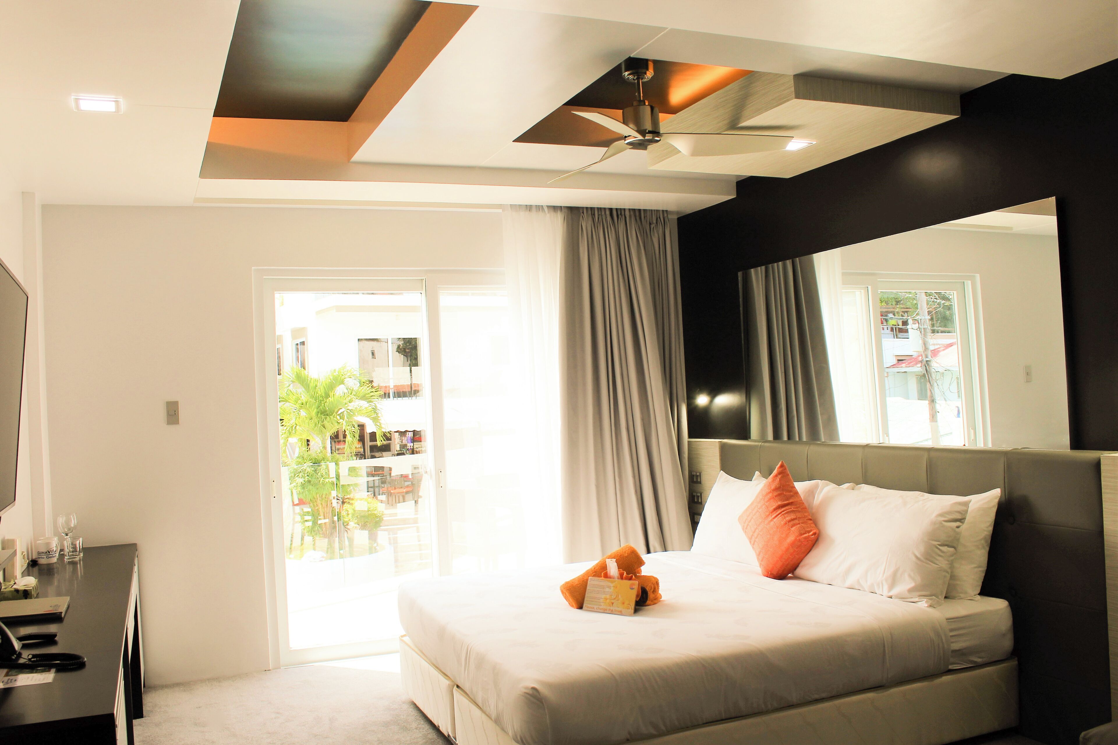 A modern hotel room with a large bed, a desk, and a ceiling fan.