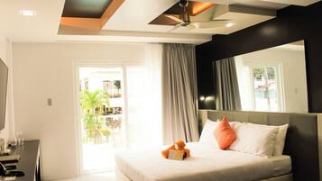A modern hotel room with a large bed, a desk, and a ceiling fan.