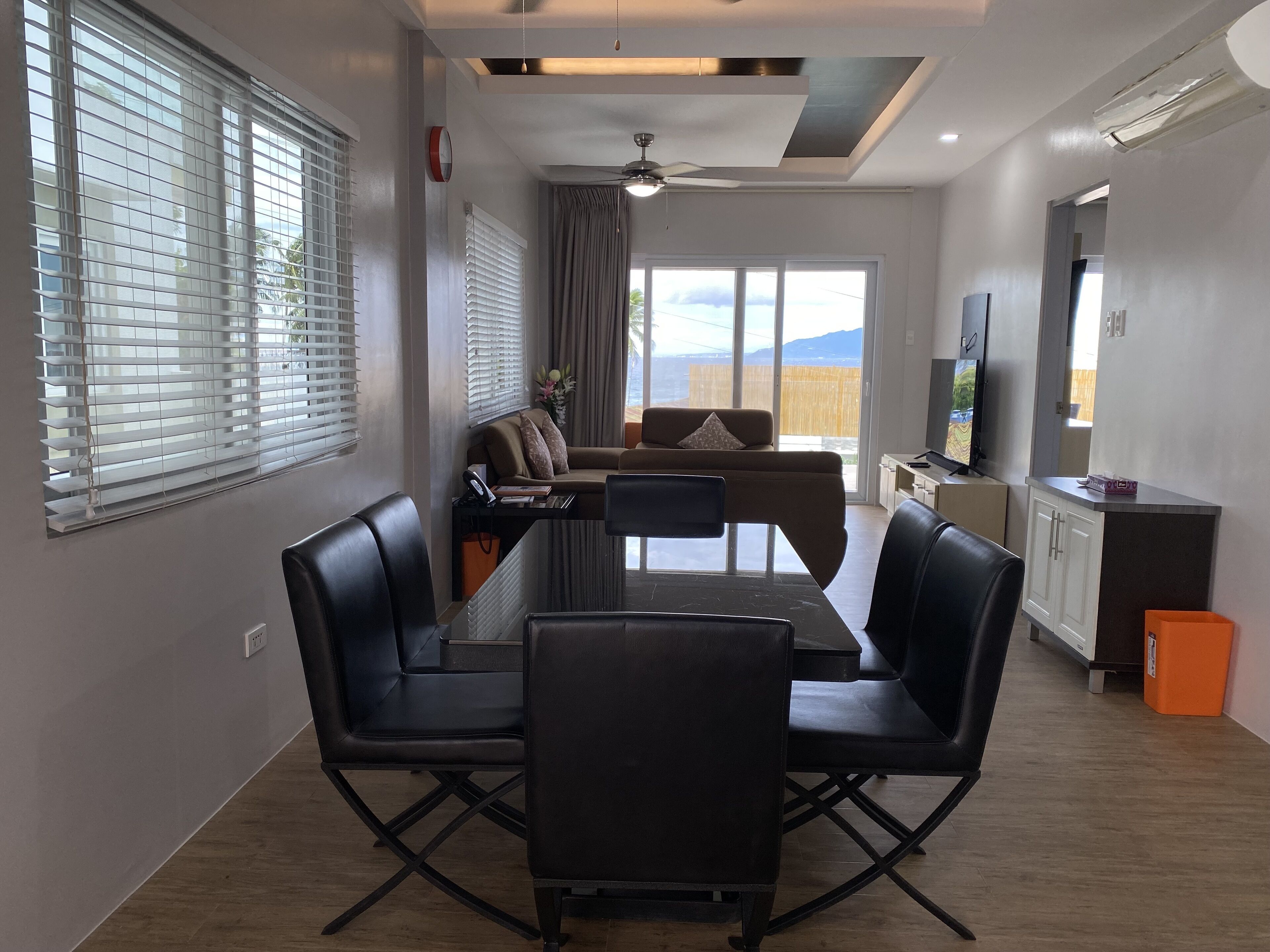 Una sala de estar moderna con una mesa de comedor, sillas de cuero negro, un sofá y una televisión.