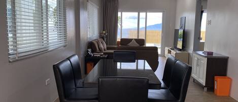 Una sala de estar moderna con una mesa de comedor, sillas de cuero negro, un sofá y una televisión.