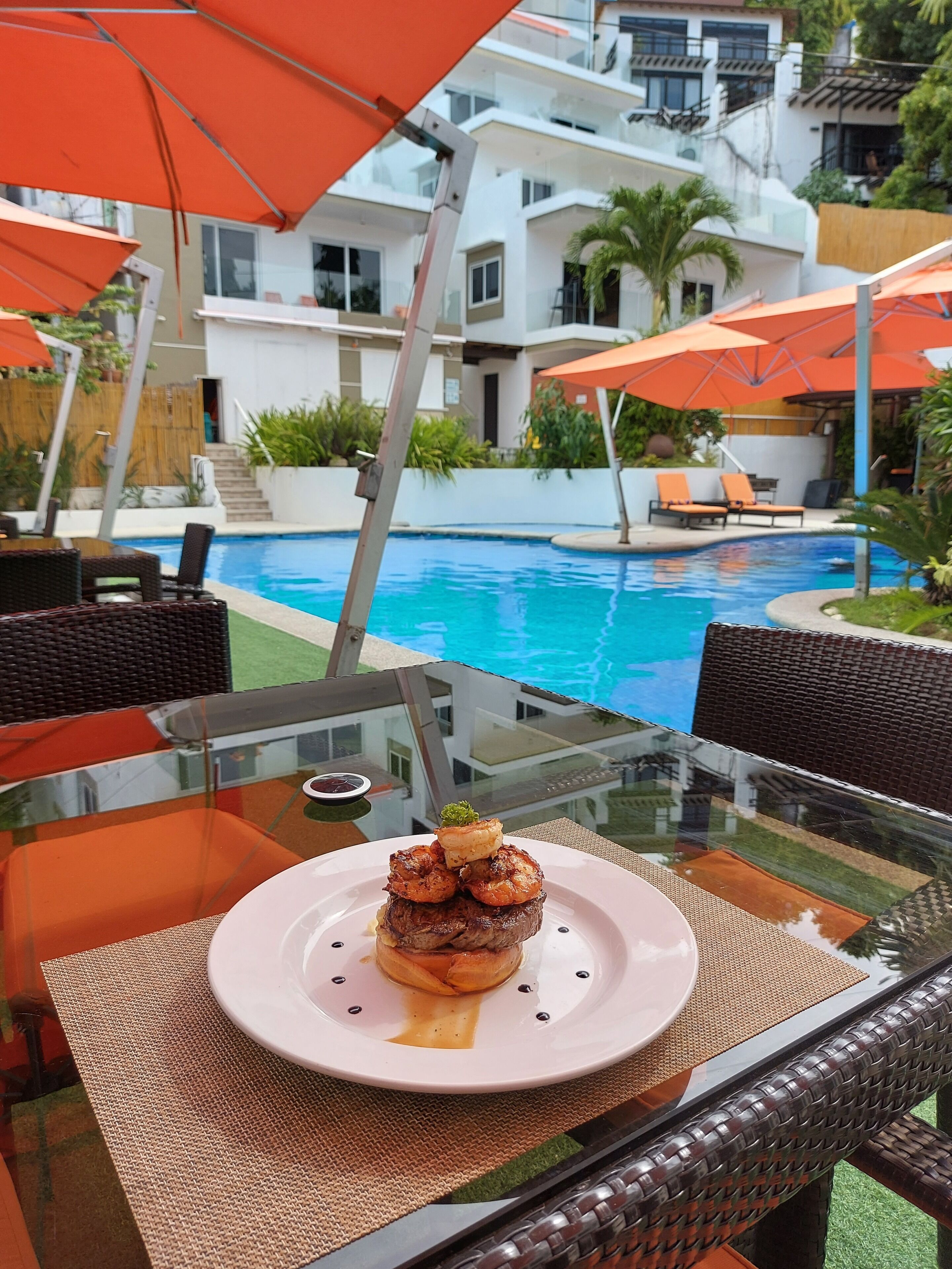 A dining table with a plate of food, a glass table, and outdoor seating with orange umbrellas.