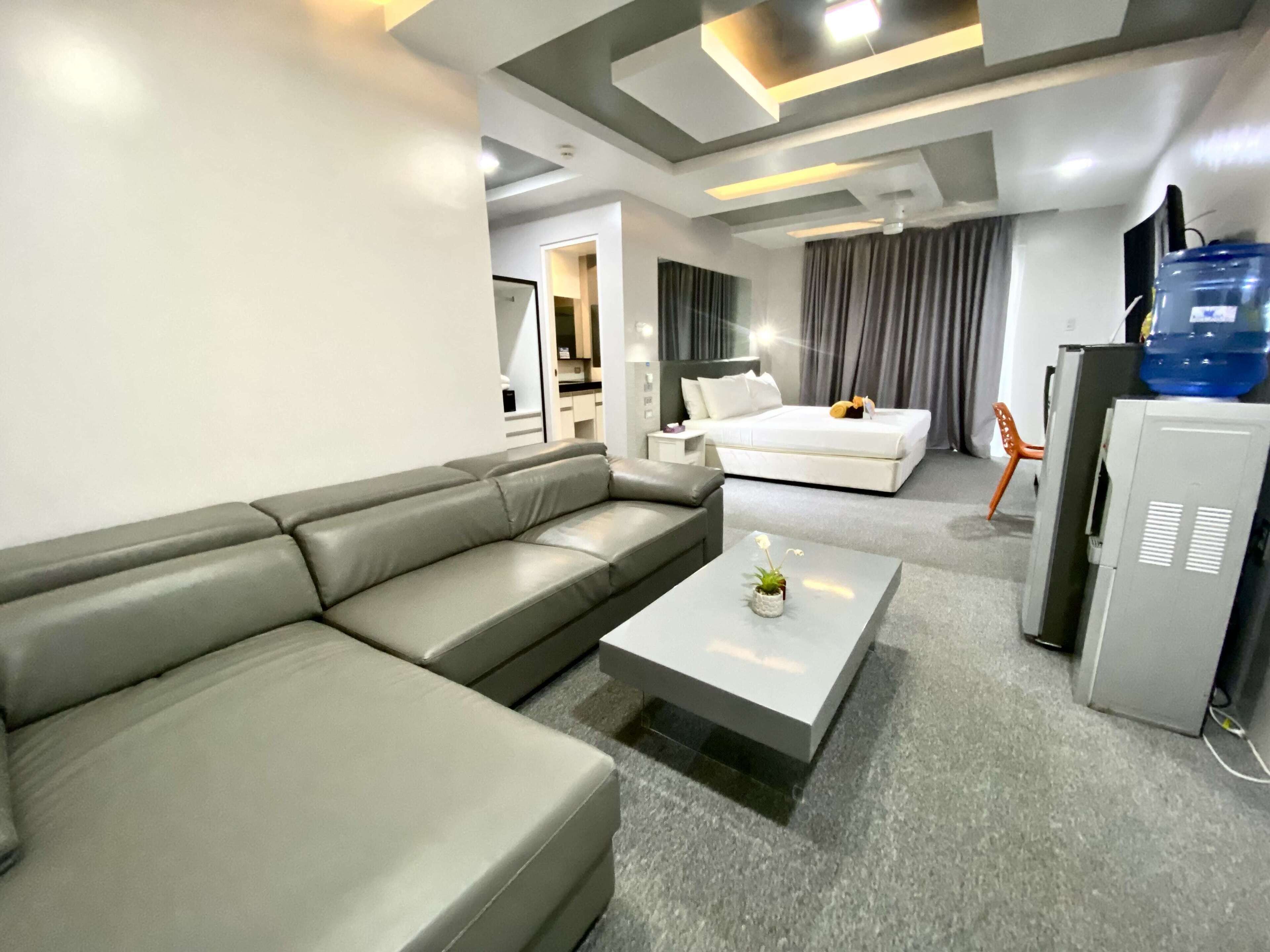 A modern living room with a grey sofa, a white coffee table, and a bed with a grey headboard.