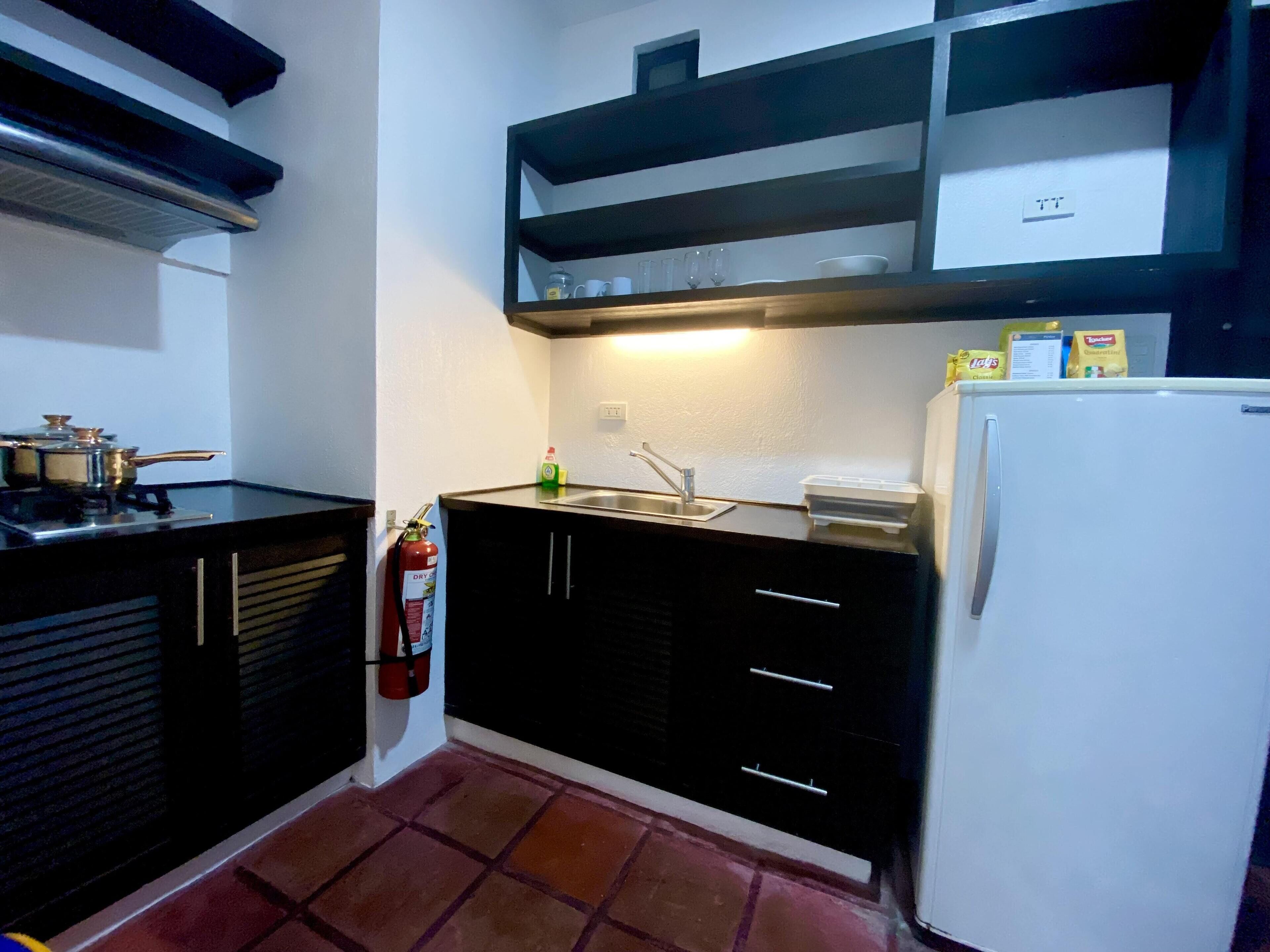 A compact kitchen with black cabinets, a white refrigerator, a gas stove, and a shelf above the sink.