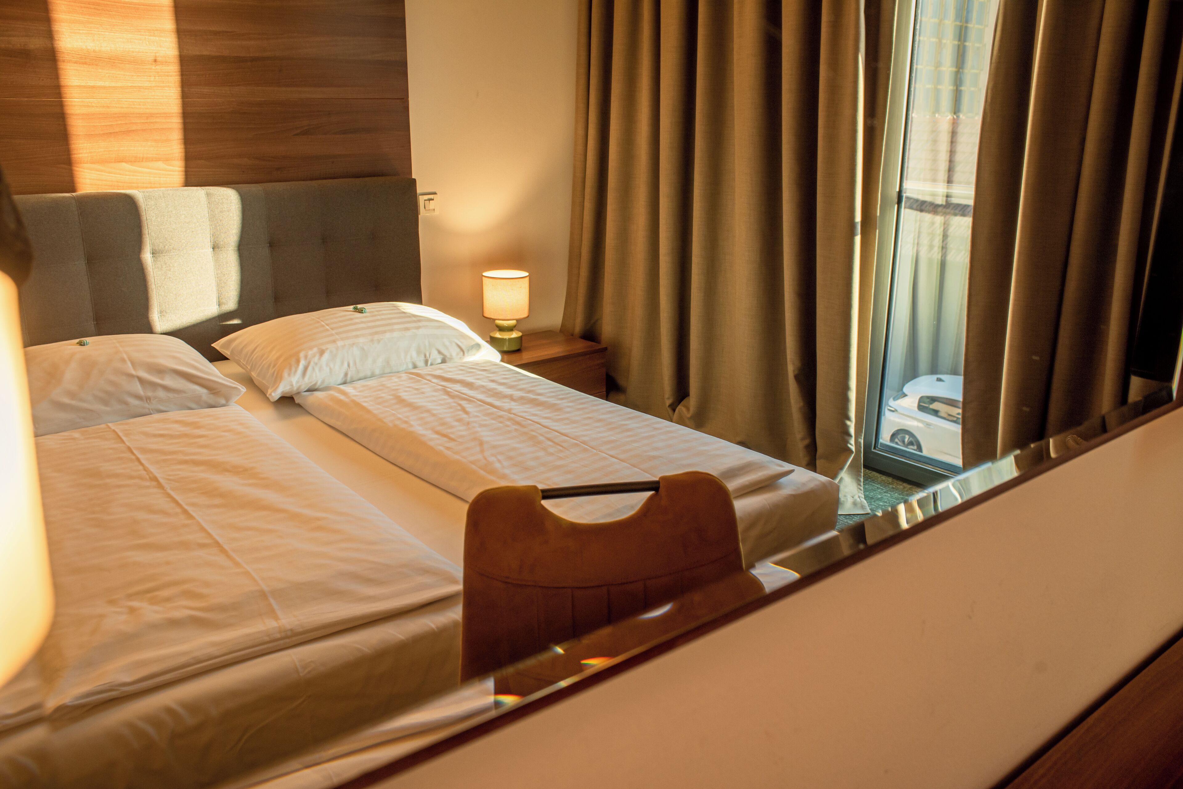 A hotel room with a bed, a nightstand, a lamp, and a window with curtains.