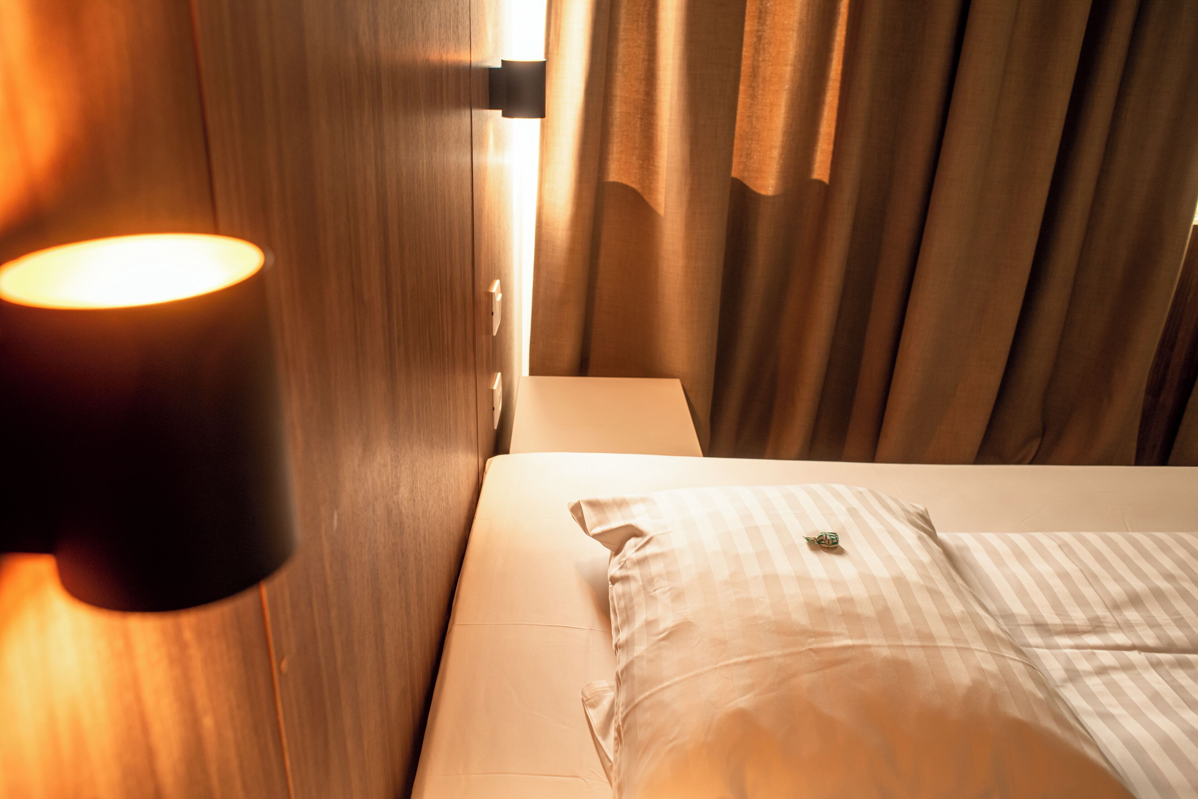 Ein Hotelzimmer mit Bett, Nachttischlampe und Vorhängen.