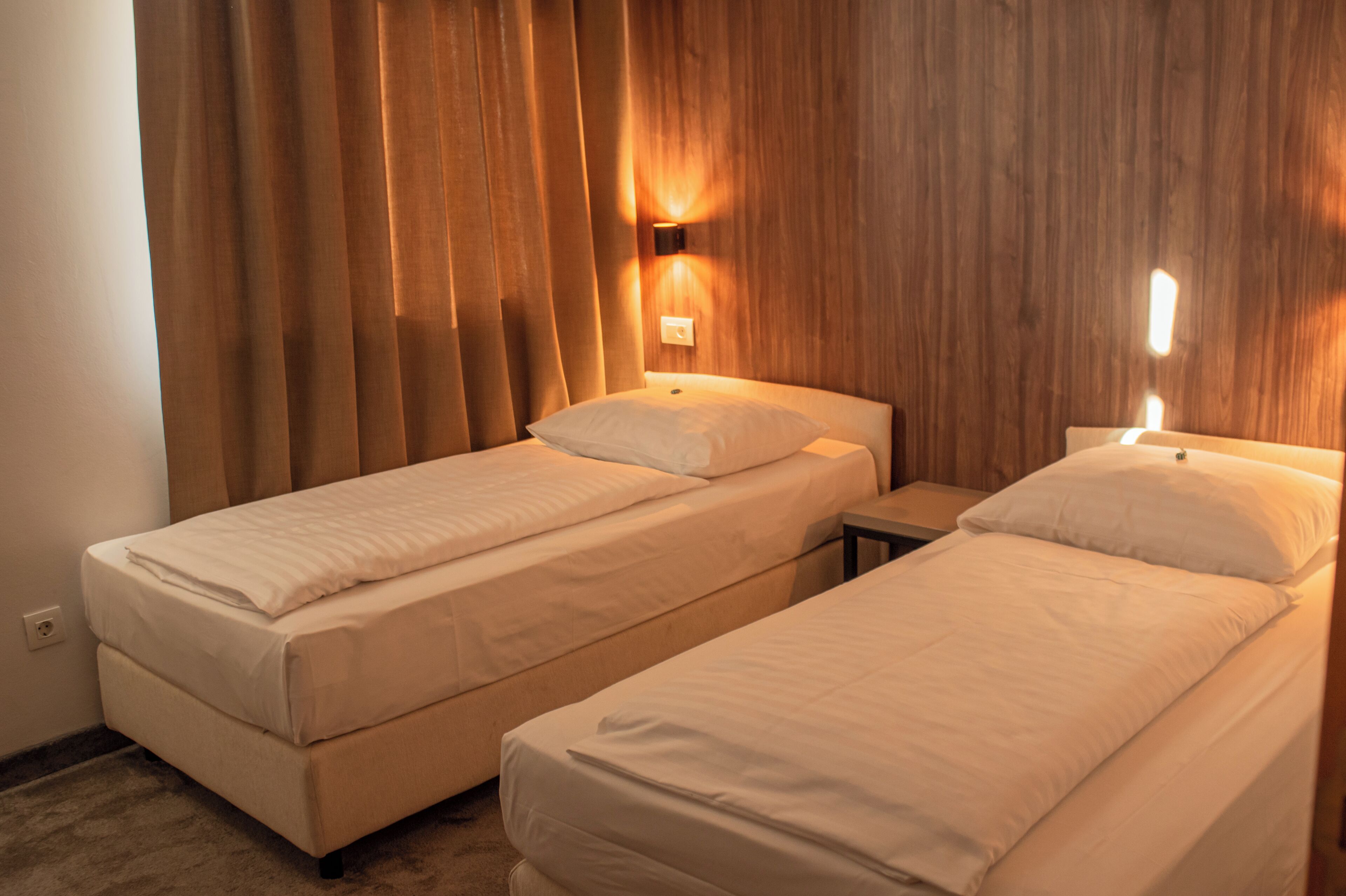 Une chambre d’hôtel avec deux lits simples, une tête de lit en bois et un luminaire fixé au mur.