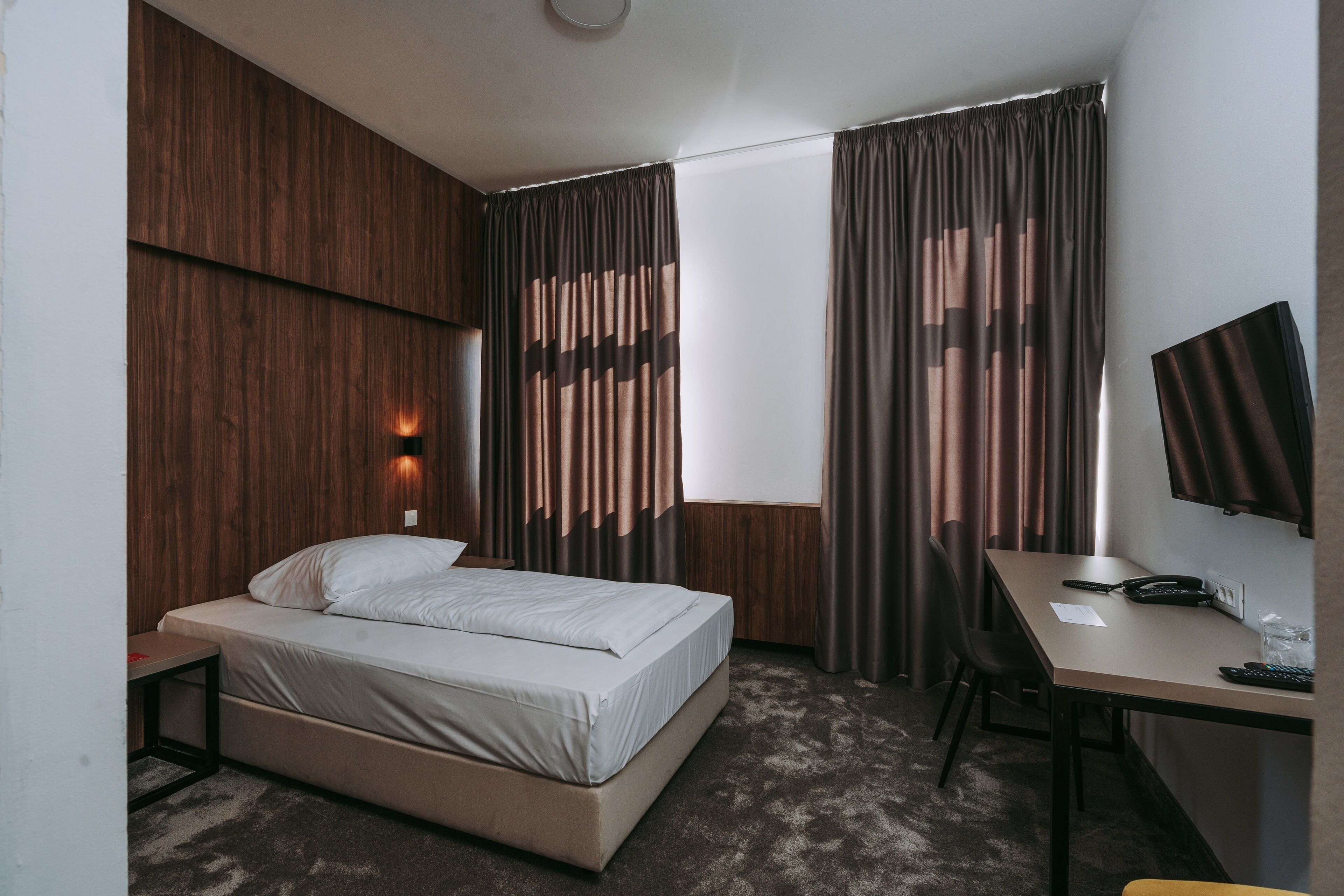 A hotel room with a bed, a desk, a chair, and a TV.