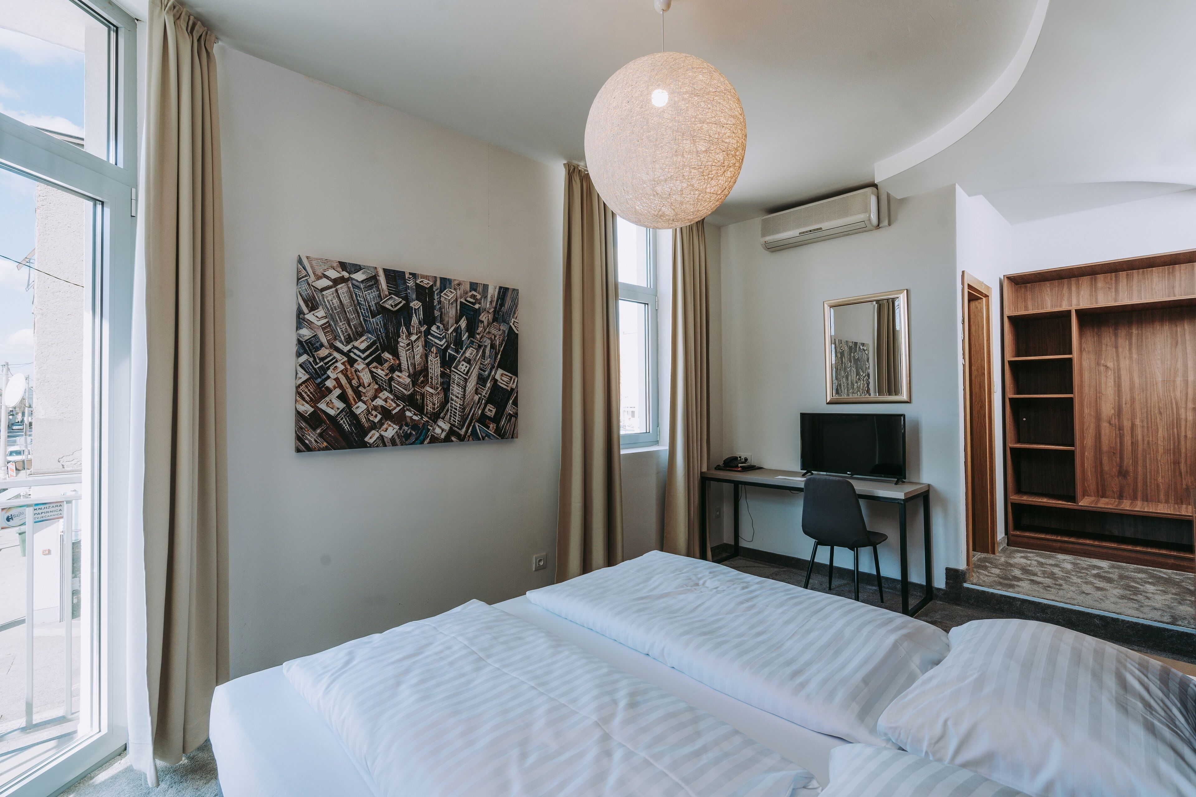 A hotel room with a bed, a desk with a computer, a television, and a wardrobe.