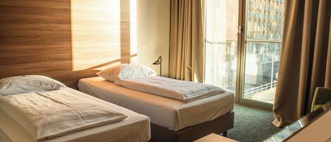 A hotel room with two beds, a desk, a chair, a lamp, and a view of the outside through a glass door.