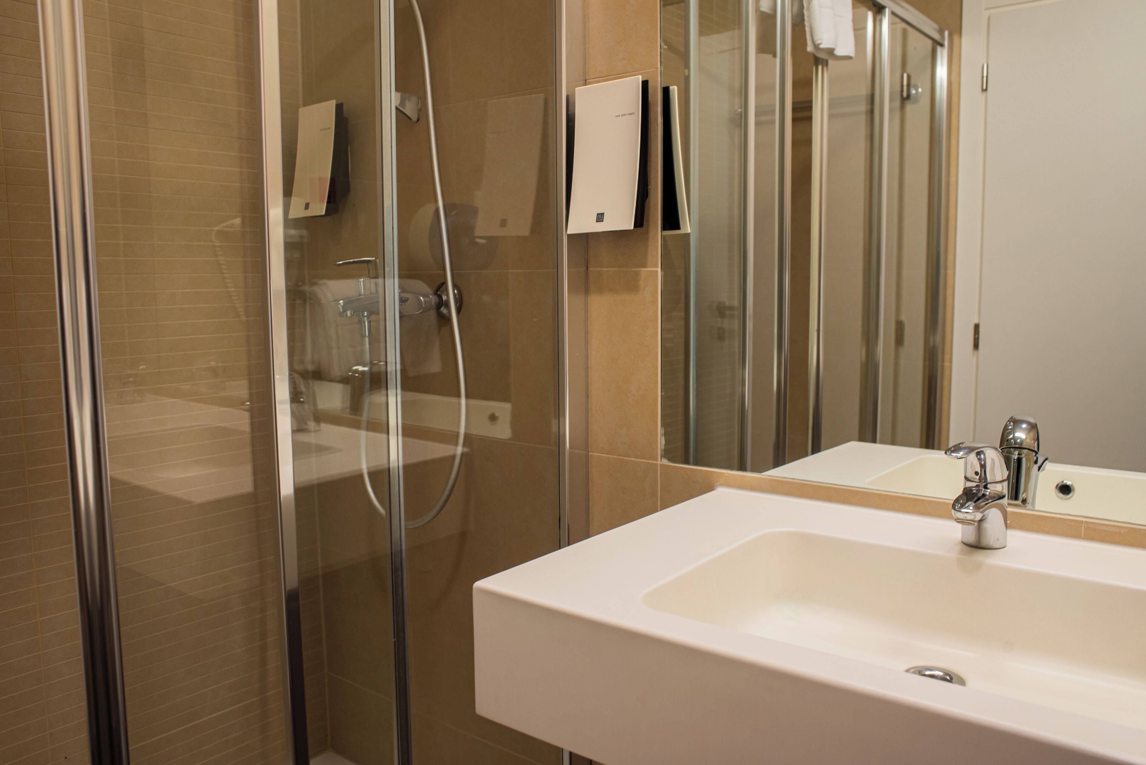 A modern bathroom with a glass shower enclosure, a white sink, and a mirror reflecting the room.