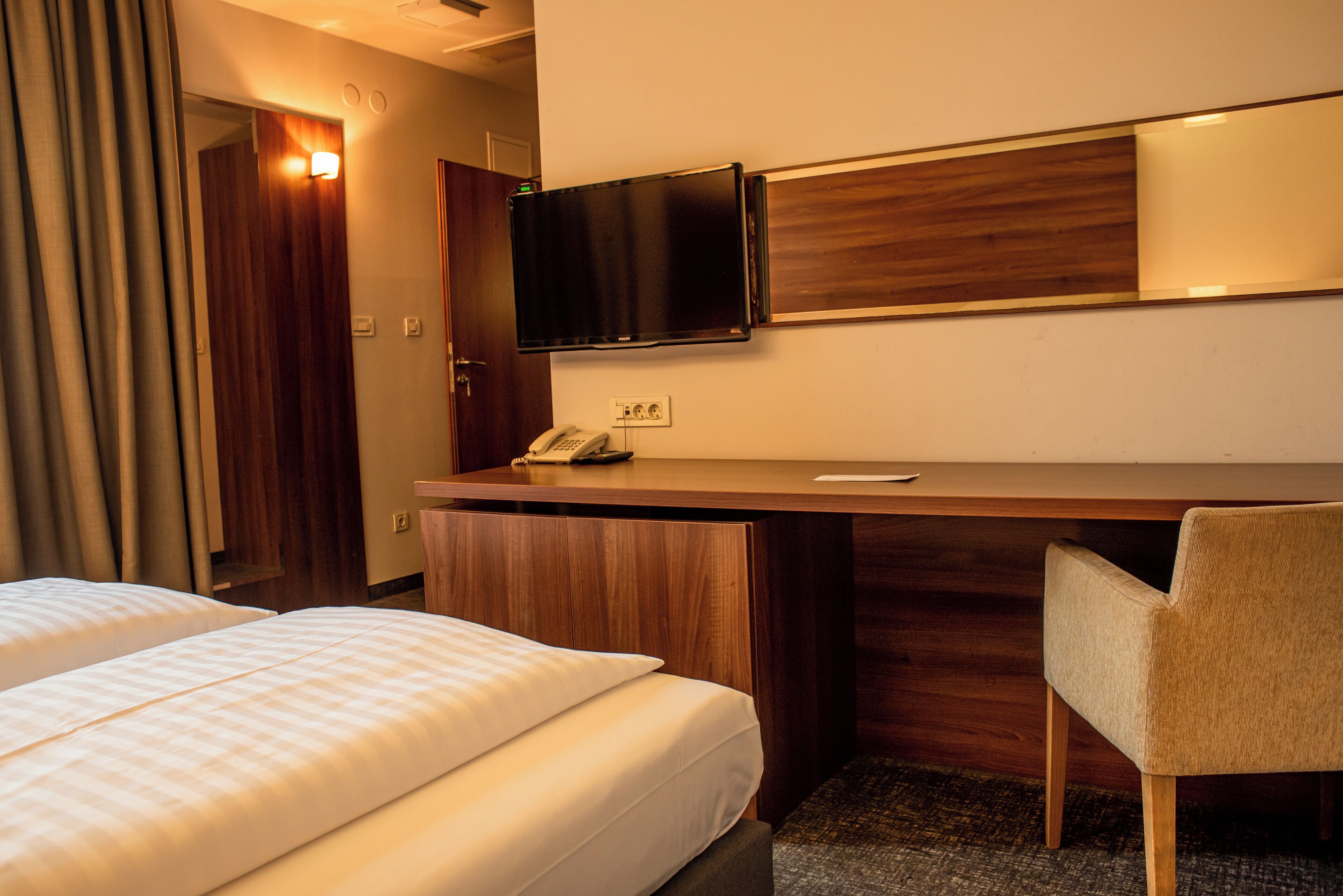 A hotel room with two beds, a desk with a telephone, and a television mounted on the wall.