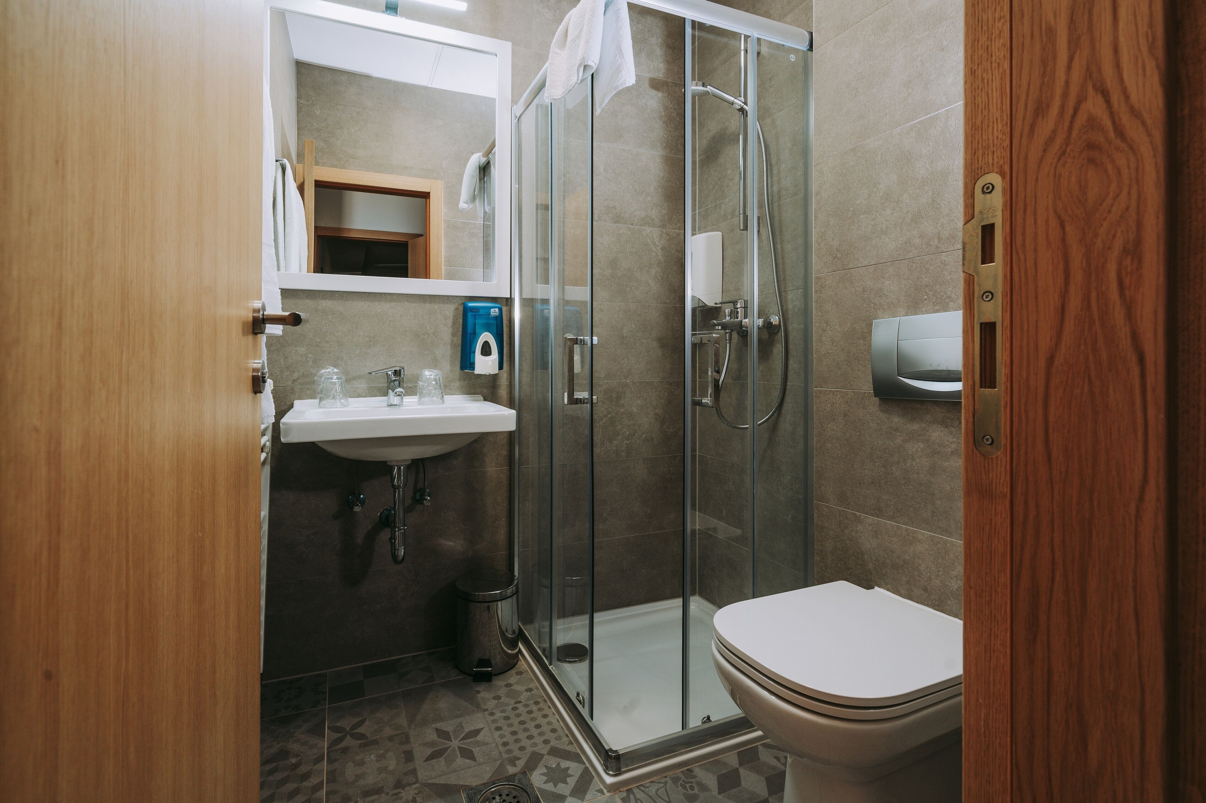 Un baño con cabina de ducha de vidrio, inodoro y lavamanos con espejo.