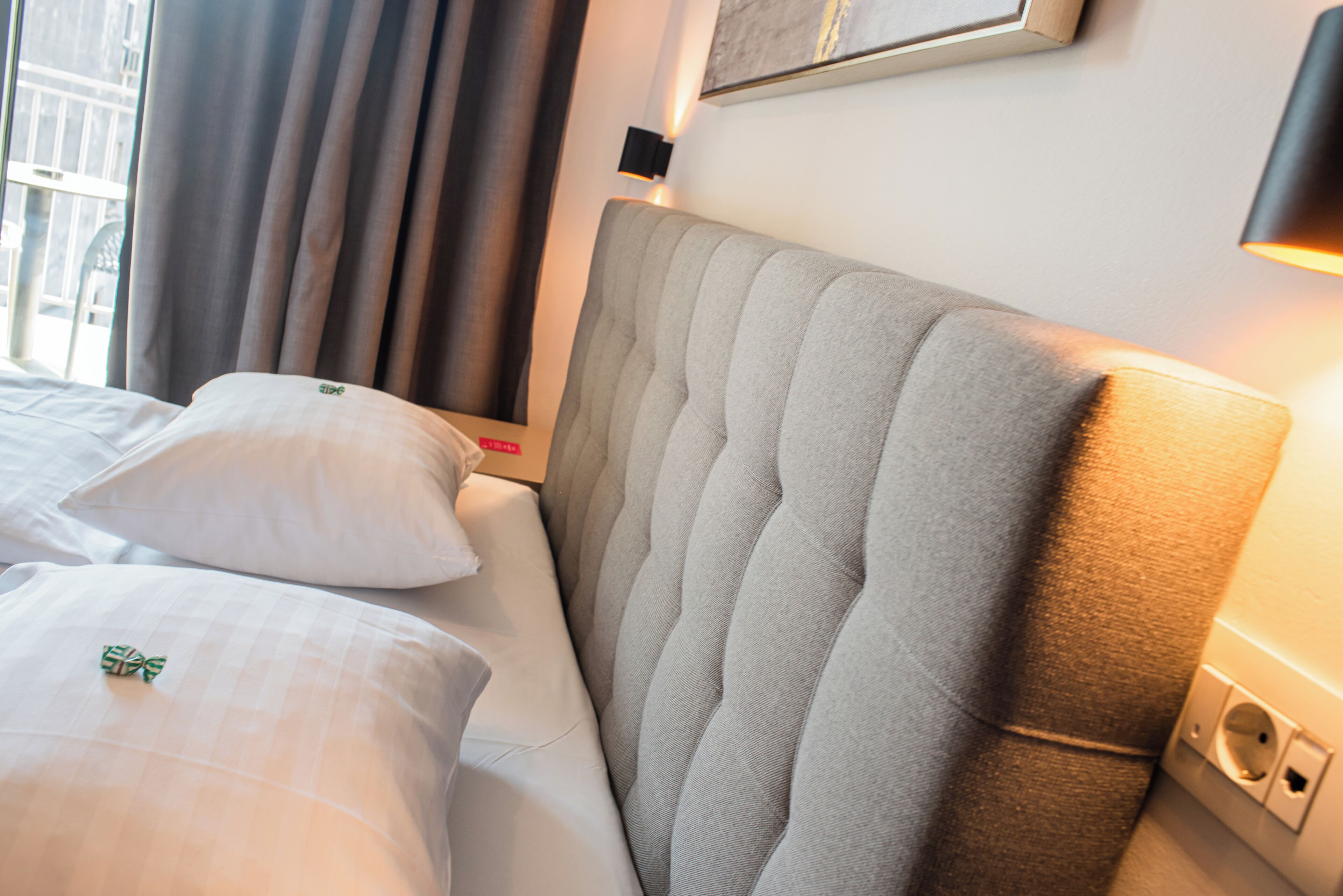 Une chambre d’hôtel avec un lit bien fait, une tête de lit et un luminaire fixé au mur.