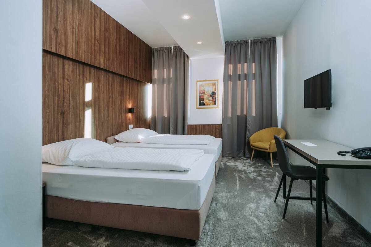 A hotel room with two beds, a desk, a chair, a TV, and a painting on the wall.