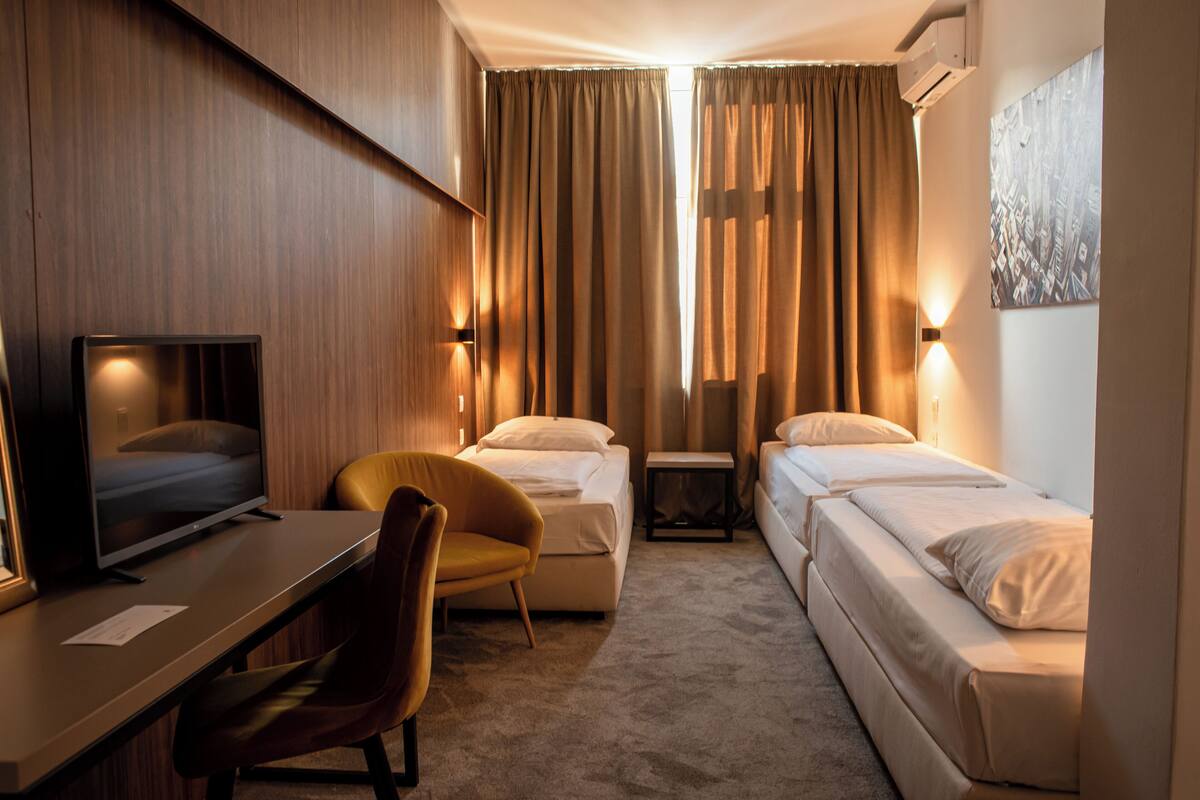A hotel room with a bed, a desk with a TV, a chair, and a small table.